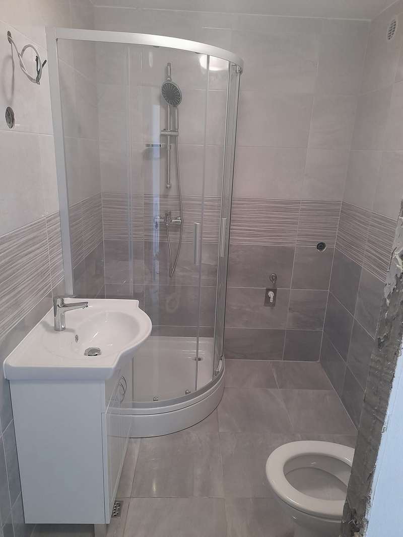 Gotova kupaonica sa sivim pločicama, zaobljenom tuš kabinom, umivaonikom i wc školjkom.