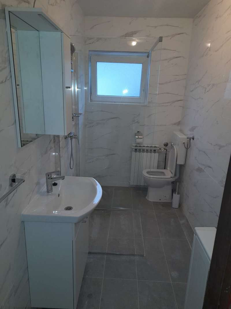Gotova kupaonica sa svijetlim pločicama, umivaonikom, tuš kadom i wc školjkom.