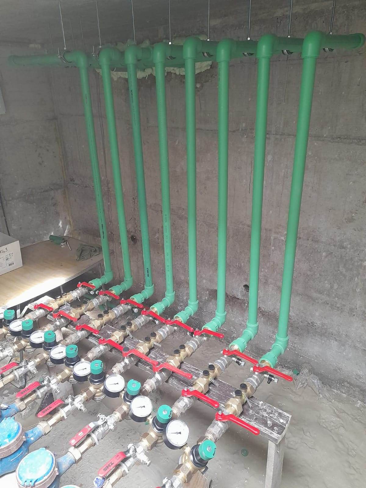 Zelene vertikale za vodu spojene na niz vodomjera s crvenim ventilima, izvedeni razvod u prostoriji s vodomjerima.